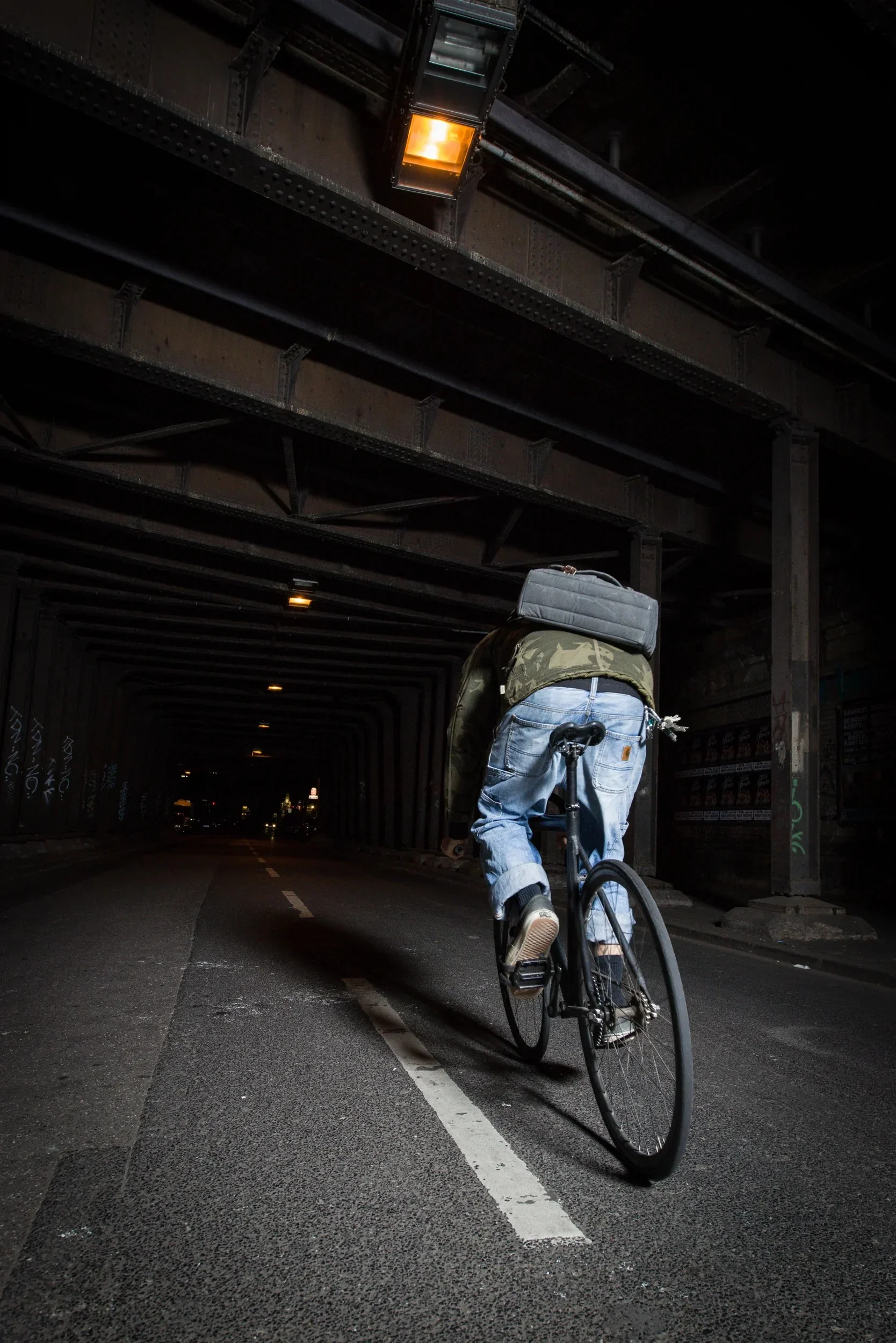 Rear view of a cyclist on a single-speed bike entering a dark urban tunnel.